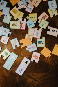 A collection of educational puzzle pieces with words and illustrations on a wooden parquet floor.